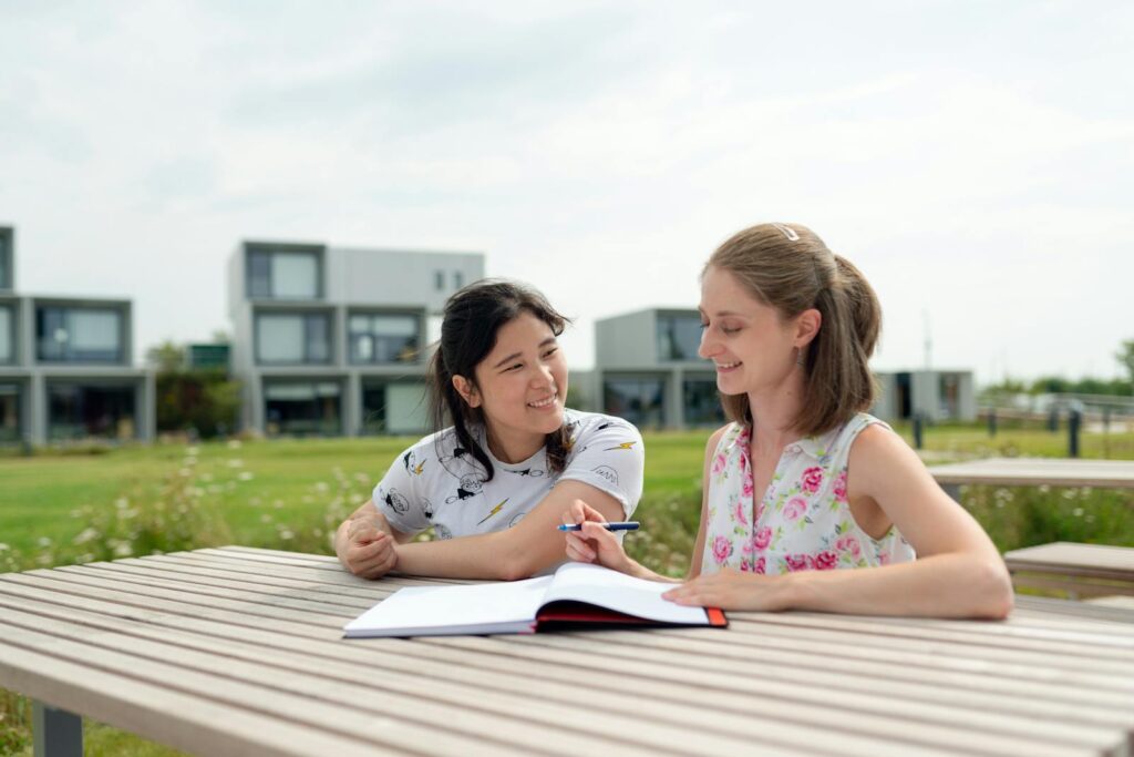 Two young women studying together outdoors on a modern campus, enjoying a sunny day.