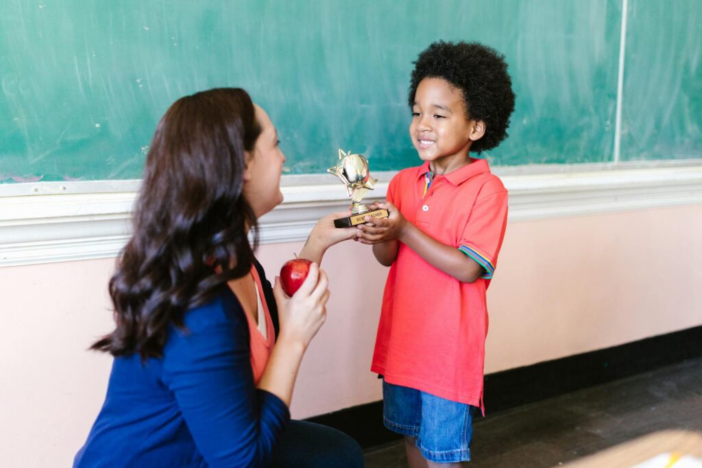 A teacher presents a trophy to a smiling child in a classroom setting.